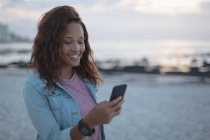 Junge Frau benutzt Handy am Strand — Stockfoto
