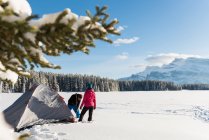 Paar schlägt im Winter sein Zelt in verschneiter Landschaft auf. — Stockfoto