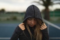 Young woman standing in hoodie at tennis court — Stock Photo