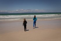 Rückansicht von Geschwistern im Neoprenanzug, die an einem sonnigen Tag in Richtung Meer laufen — Stockfoto