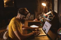 Чоловік сидить на стільці в гарнітурі віртуальної реальності, використовуючи свій ноутбук вдома — стокове фото