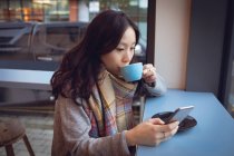 Hermosa mujer usando el teléfono móvil mientras toma café en la cafetería - foto de stock