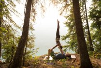 Pareja deportiva practicando acro yoga en un frondoso bosque verde a la hora del amanecer - foto de stock