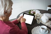Mujer mayor usando tableta en la sala de estar en casa - foto de stock