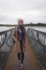 Mulher atenciosa em roupas quentes em pé na ponte — Fotografia de Stock