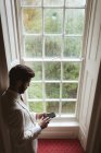 Groom usando seu telefone celular perto da janela em casa — Fotografia de Stock