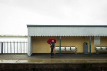 Junge Frau steht mit Regenschirm am Bahnhof — Stockfoto