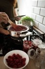 Mediados de sección abuela y nieta cocinar mermelada de frambuesa en la cocina en casa - foto de stock