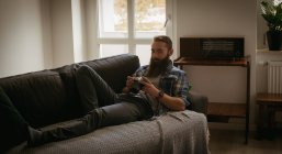 Человек рассматривает изображение на цифровой камере, расслабляясь на диване — стоковое фото