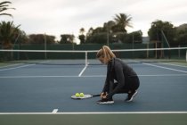 Молодая женщина завязывает шнурки на теннисном корте — стоковое фото
