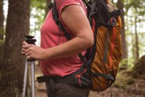 Mid section of mature woman with hiking poles standing in the forest — Stock Photo