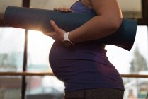 Sección media de la mujer embarazada que sostiene la esterilla de ejercicio en casa - foto de stock