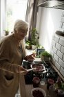 Усміхнена старша жінка готує малинове варення на кухні вдома — стокове фото