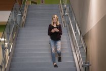 Adolescente utilisant un téléphone mobile sur un escalier à l'université — Photo de stock
