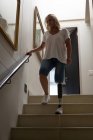 Femme mûre avec la jambe prothétique descendant les escaliers à la maison . — Photo de stock