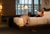 Бізнес-леді, сидячи на ліжку, тримає документи під час використання мобільного телефону в готелі — стокове фото