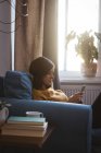 Jeune femme se relaxant sur le canapé en utilisant son téléphone portable dans le salon à la maison — Photo de stock
