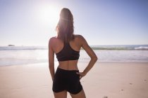Adatto donna in piedi con mano sul fianco in spiaggia al crepuscolo, vista posteriore . — Foto stock