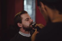 Al hombre le cortan la barba con una podadora en la barbería. - foto de stock