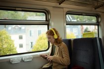 Junge Frau hört Musik, während sie Tablet im Zug benutzt — Stockfoto