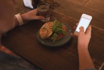Seção média de mulher usando celular enquanto toma café da manhã à mesa no café — Fotografia de Stock