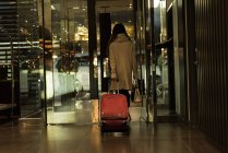 Vista trasera de la mujer de negocios saliendo de la habitación del hotel con equipaje - foto de stock