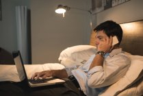 Empresário usando laptop enquanto fala no celular no quarto — Fotografia de Stock