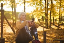 Старшая женщина использует свой мобильный телефон в парке в солнечный день — стоковое фото