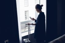 Woman with luggage using mobile phone in hotel room — Stock Photo