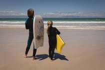 Vista posteriore dei fratelli in muta in piedi con tavola da surf sulla spiaggia — Foto stock
