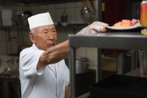 Senior chef holding plate of sushi in kitchen at restauant — Stock Photo