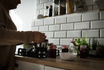 Средняя часть пожилой женщины готовит малиновое варенье на кухне дома — стоковое фото