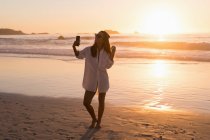 Donna che prende selfie con il cellulare in spiaggia al tramonto . — Foto stock