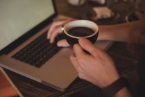 Primer plano del hombre que usa el ordenador portátil mientras toma café en la cafetería - foto de stock