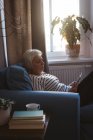 Senior mulher sentada no sofá usando seu tablet na sala de estar em casa — Fotografia de Stock