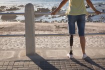 Disabled woman standing by beach in sunlight, rear view. — Stock Photo