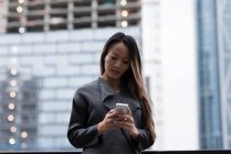 Donna d'affari utilizzando il suo telefono cellulare in piedi contro l'edificio della città — Foto stock