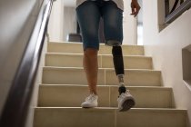 Обрізаний вид жінки з протезною ногою, що рухається вниз по сходах вдома . — стокове фото