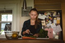 Девушка стоит на кухне и режет овощи ножом дома . — стоковое фото