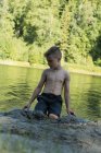Niño jugando con arena cerca de la orilla del río en un día soleado - foto de stock