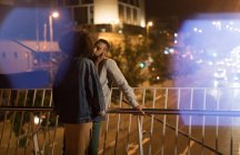 Romantisches Paar küsst sich, während es nachts am Geländer steht — Stockfoto