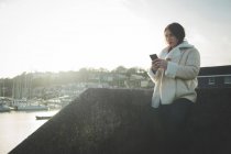 Frau benutzt Handy in Ufernähe im Sonnenlicht. — Stockfoto