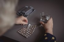 Mid section of woman sitting with pills and glass of water — Stock Photo