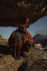 Masai homme en vêtements traditionnels assis avec bâton sur le rocher — Photo de stock