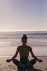 Mujer en forma meditando en la playa al atardecer . - foto de stock