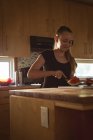 Mädchen steht in Küche und schneidet Wassermelone mit Messer. — Stockfoto