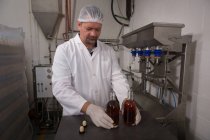 Operaio di sesso maschile che tiene gin in bottiglia in fabbrica — Foto stock