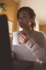 Donna che usa il computer portatile mentre prende il caffè a casa — Foto stock