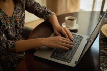 Partie médiane de la femme travaillant sur ordinateur portable avec du café — Photo de stock