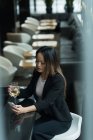 Femme d'affaires asiatique tenant une coupe de champagne tout en utilisant son téléphone portable dans le hall — Photo de stock